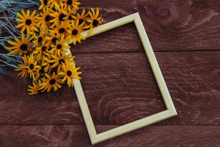 Empty photo frame with a bouquet of summer yellow daisies with a black middle, Echinacea on a brown wooden background with an empty space for text view from the top for greetingsの写真素材