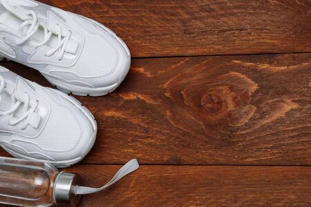 A pair of women's white and new sneakers with a clear sports water bottle on a brown wooden background with an empty space for text top viewの写真素材