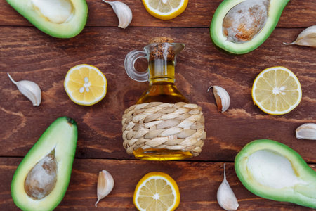 Olive oil in a glass bottle in a wicker case with lemon slices, garlic and halves of ripe avocado on...