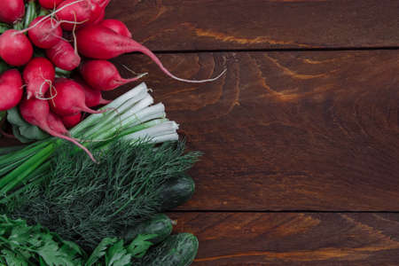 Vegetables, radishes, cucumbers and a bunch of green onions and dill on a brown wooden background top view with an empty space for text, the concept of summer vegetables and cooking, diet foodの写真素材