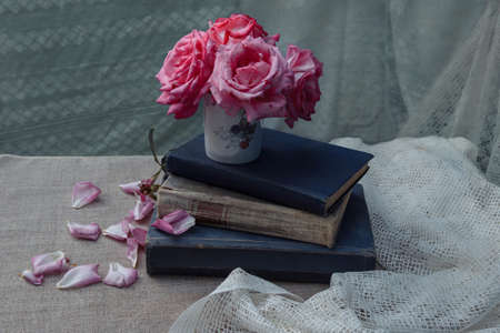 bouquet of pink roses in a mug with old books on the table on a light background with white tulle, the concept of retro still life, vintage and rusticの写真素材