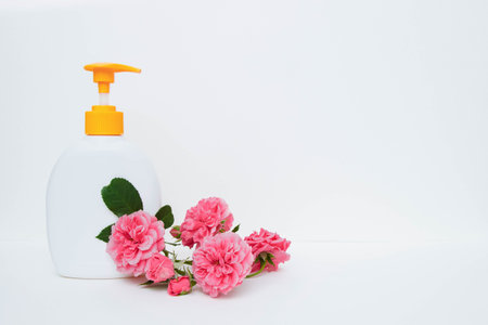 Empty plastic bottle with liquid soap and yellow dispenser, bouquet of pink roses on a white...