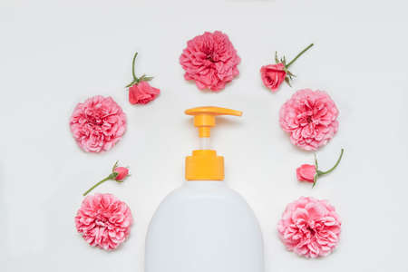 White plastic bottle with dispenser close-up with pink flowers and rosebuds on a white isolated background top view, close-up, skin care concept, hair Care, soap and balms, empty space for textの写真素材