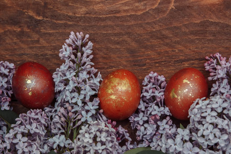 Easter painted eggs brown with gold on a brown wooden background with lilac flowers close-up with an...