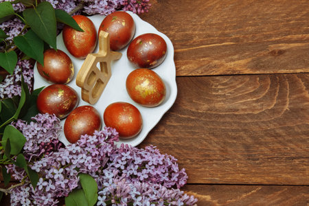 Easter painted eggs on a white plate with lilac flowers on a brown wooden background top view with empty space for text, greeting card concept, religious traditions, Christian holidayの写真素材