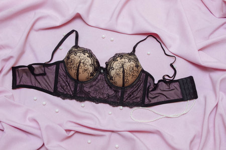 Black lace bra on pink bed fabric with white pearls close-up top view of flat composition, Valentine's day celebration concept, fashionable and sexy underwear, romantic evening and night, dateの写真素材