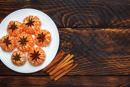 angerines in a white plate with star anise and cinnamon on a brown wooden background with an empty space for text, the concept of Christmas, ingredients for warming seasonal drinks and mulled wineの写真素材