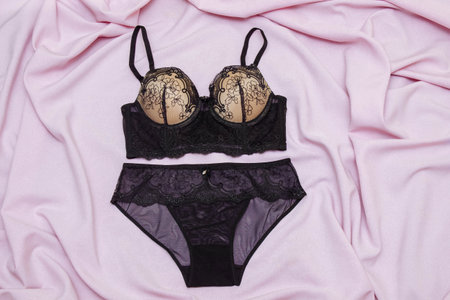 Set of women's lace underwear in black bra and panties on a pink background, fabric with pleats, the concept of fashionable, comfortable and seductive clothes and preparation for a date, health careの写真素材