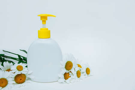 White plastic bottle with dispenser on light background with chamomile flowers with empty space for text, copy space, concept of natural organic cosmetics, skin, body and hair care, hand soapの写真素材