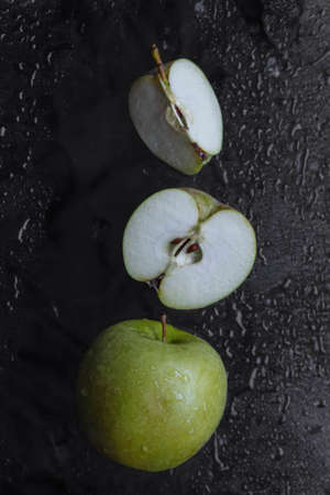 whole green apple, cut in half and quarters on black background with water drops with noise, grain and film effect, blurred, out of focus, flat lay, dark mood concept, vitamins and label addの写真素材