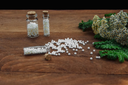Glass bottles with white pills dragees with chamomile flowers and green herbal leaves on black...