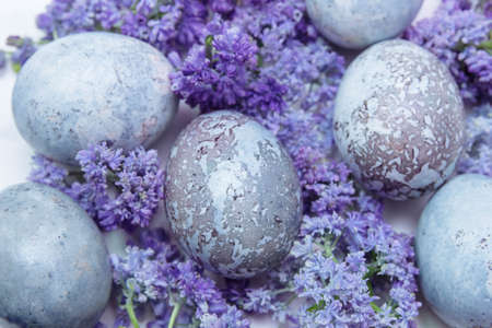 Painted, decorated Easter eggs blue and lilac with purple muscari and lilac flowers close-up on a white background, spring holiday concept, greeting cards, traditions of Christianity and Orthodoxyの写真素材