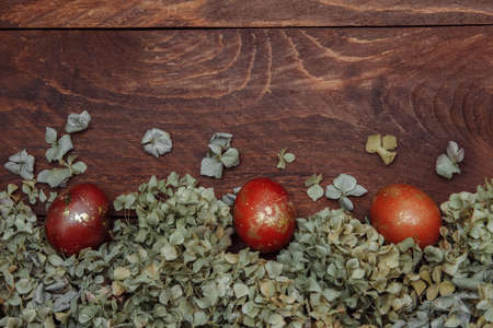 Red-brown and gold abstract eggs painted on brown wooden background with empty space for text, copy space, top view, flat lay, with dried hydrangea flowers, greeting card concept, template designの写真素材