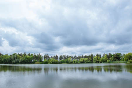 Spring landscape out of focus with noise, grain and film effect with big lake, forest trees, pines and willows with clouds before rain, tourism concept, countryside, wallpaper and coverの写真素材