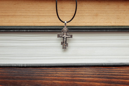 Christian crucifixion close-up out of focus against the background of old closed books, the Bible, the Gospel, on a wooden table, the concept of faith, hope, prayer, confession and forgiveness of sinの写真素材