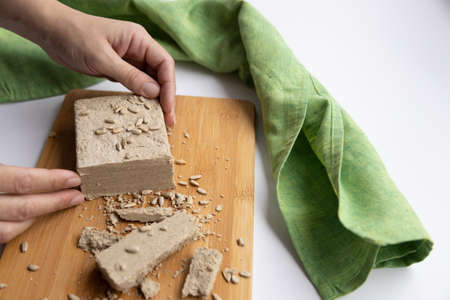 a woman holds a sunflower halva on a wooden board with sunflower seeds in her handsの写真素材