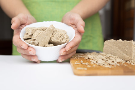 a woman holds a sunflower halva on a wooden board with sunflower seeds in her handsの写真素材