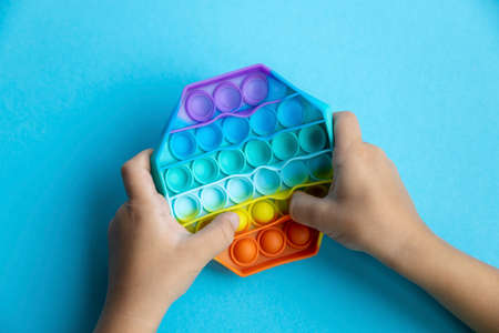 Popular new fashionable Pop IT toy for children and people with stress on a blue background. Rainbow Bubble Toy For Kids. The hands of a child. copy spaceの写真素材