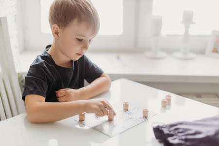 a lotto game. A boy child is playing a lotto game at a white table on a light background.の写真素材