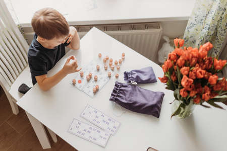 a lotto game. A boy child is playing a lotto game at a white table on a light background.の写真素材