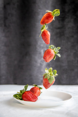 strawberries in weightlessness on a dark background over a white plateの写真素材