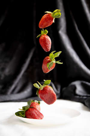 strawberries in weightlessness on a dark background over a white plateの写真素材