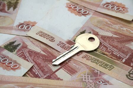 Metal key on a horizontal background of a variety of banknotes of five thousand Russian rubles. Concept of buying an apartment, flat or house, mortgage, rental housing, housewarming, home expenseの写真素材