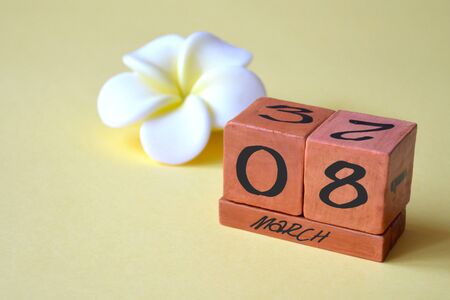 A wooden perpetual calendar with March 8 and a white with yellow flower on a yellow background with copy space. Concept of holiday, spring, mother's day, international women's dayの写真素材
