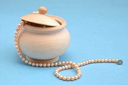 Light wooden sugar bowl with a lid and a string of sea pink pearls on a blue background. Wooden unpainted barrel preparation for creativityの写真素材