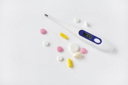Multi-colored pills and an electronic thermometer with a temperature of 36.6 on a white backgroundの写真素材