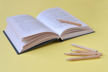 Opened book and wooden pencils on a yellow background with copy space. Concept of education,...