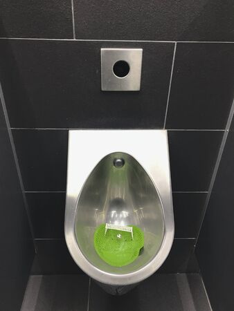 Interior of a public male restroom in dark gray tones. Original urinal with miniature football goal and ball. WC for football fans. Top viewの写真素材