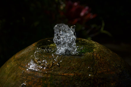 Close up of a small fountain of water in motion from a round stone against a dark background