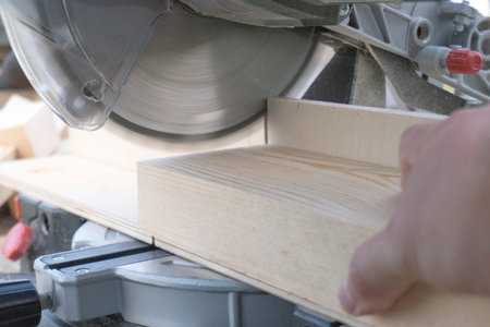 Close-up of a carpenter working with a miter saw to cut a piece of pine wood. Concept of...