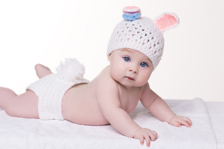 cute baby girl 4 - 5 months lying naked on a white blanket wearing a hat in the form of bunny with ears and tailの写真素材