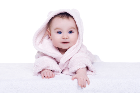 cute baby child in pink bathrobe hood lying down and try crawl, isolated. baby with blue eyes smiling and looking into the camera. happy family conceptの写真素材