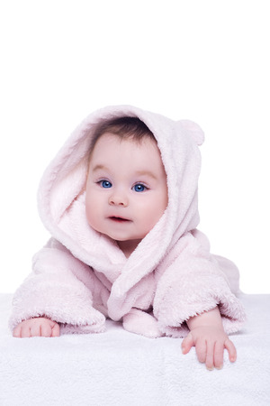 cute baby child in pink bathrobe hood lying down and try crawl, isolated. baby with blue eyes smiling and looking into the camera. happy family conceptの写真素材