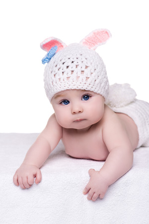 cute baby girl lying naked on a white blanket wearing a hat in the form of bunny with ears and tail. child with big blue eyes about four - five monthの写真素材