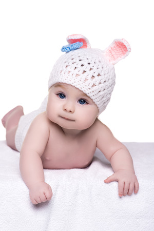 portrait of cute little baby child on white background, isolated. baby lying naked wearing a hat/cap in the form bunny. kid with big blue eyes about four - five monthの写真素材