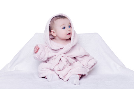 cute baby sitting on a chair in pink bathrobe with hood and with surprise looks aside. child about five month with big blue eyes and long eyelashes on whiteの写真素材