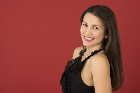 young girl on red background in black dress. beautiful brunette woman smiling and looking into the camera. beauty and fashion. model in the right cornerの写真素材