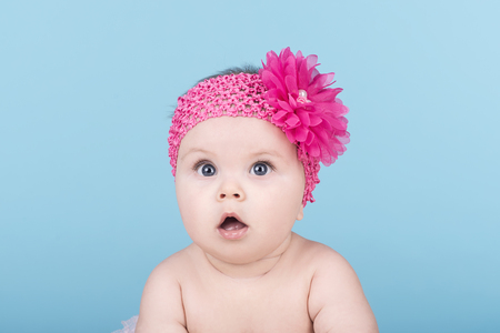 portrait of cute baby with pink bow flower on her head. surprised baby child looking into the camera. lovely kid with big blue eyes. happy family conceptの写真素材
