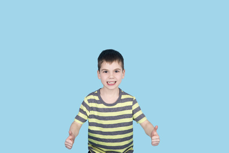 teenager boy smiling and looking into camera on blue background, isolated. kid showing thumb upの写真素材