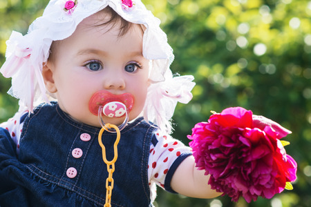 cute little baby girl looking on the flower in her hand. child with big blue eyes in a summer hat on the nature, outdoorの写真素材
