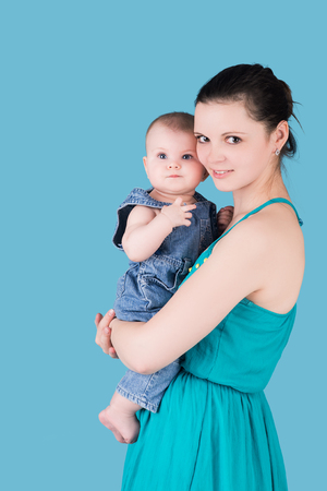 smiling young mother holding her cute baby child isolated on blue. happy family conceptの写真素材
