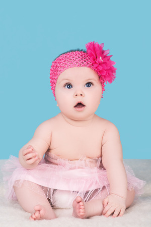 cute baby girl with pink bow flower on her head, isolated on blue. surprised child with big blue eyes look awayの写真素材