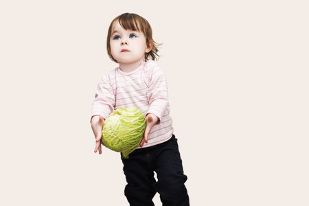 cute little baby girl with blue eyes carries cabbage in hands, isolated backgroundの写真素材