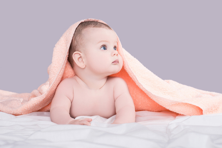 Surprised baby with big blue eyes lying on belly under the pink towel after bath, isolated over gray backgroundの写真素材