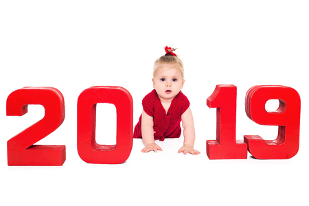 Surprised little baby girl with big blue eyes in a red dress crawls into the red numbers of 2019 year, isolated over white backgroundの写真素材