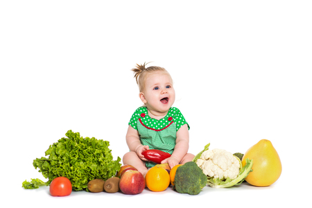Smiling baby girl sitting surrounded by fruits and vegetables, isolated over white background. The concept of healthy food and happy lifeの写真素材